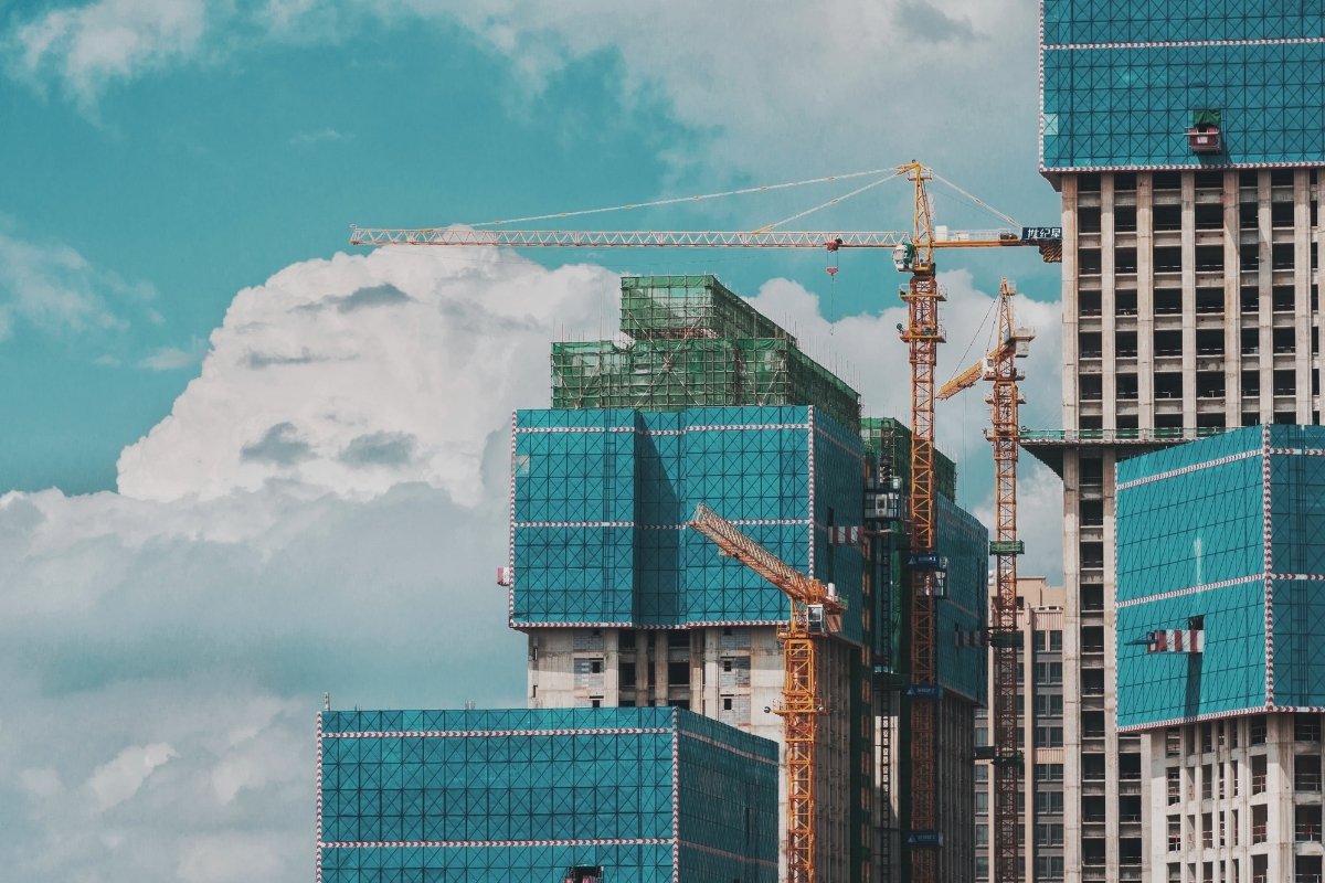 A photograph of skyscrapers set against the sky, with large glassy windows and cranes visible in the foreground