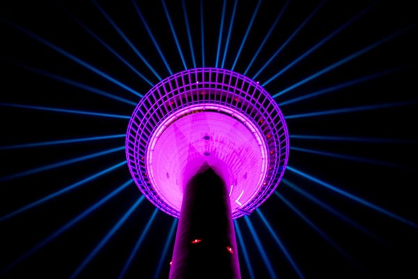 A shot from below of a tower at night, lit up in bright purple against the dark sky