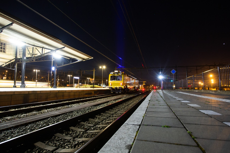 Night view of illuminated train station platform with yellow train on tracks under dark sky