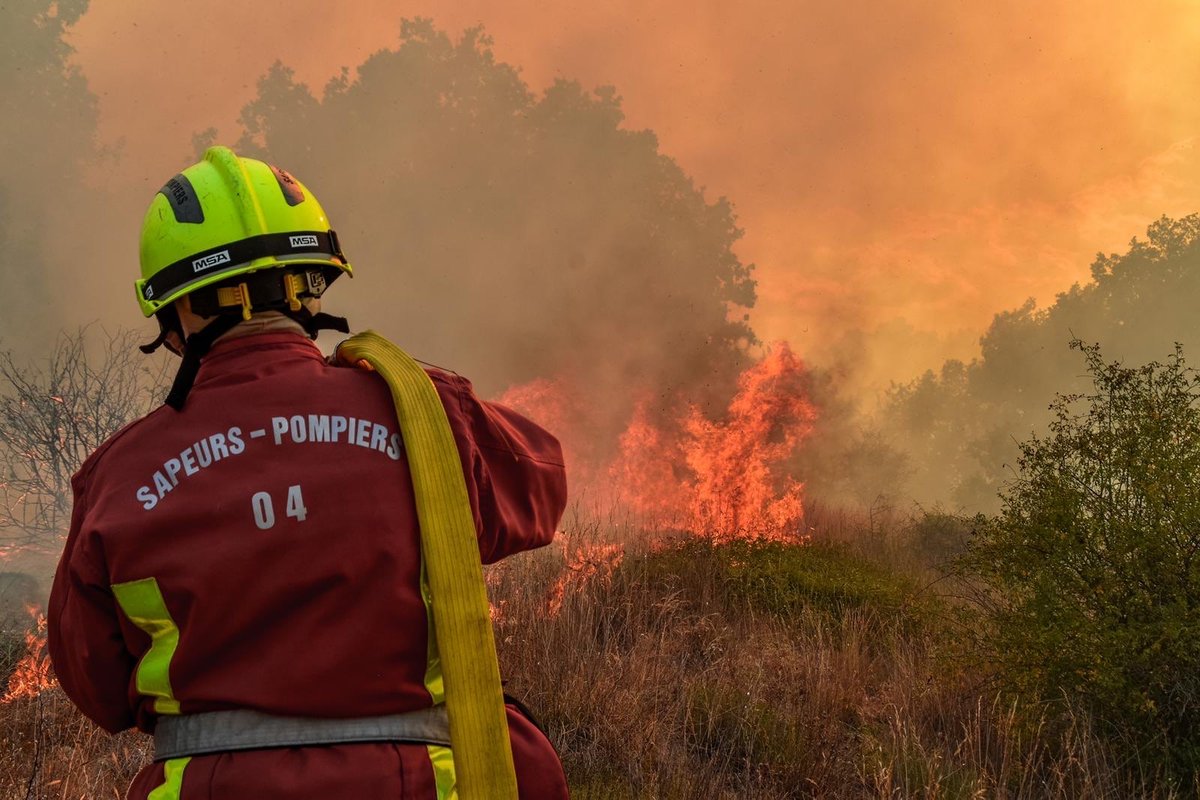 French firefighter from Sapeurs-Pompiers 04 battling wildfire with flames consuming vegetation