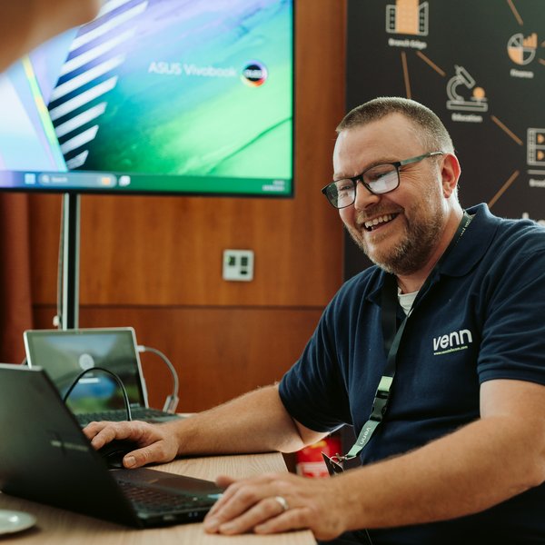 Professional expert smiling while working on laptop in modern conference room with digital display.