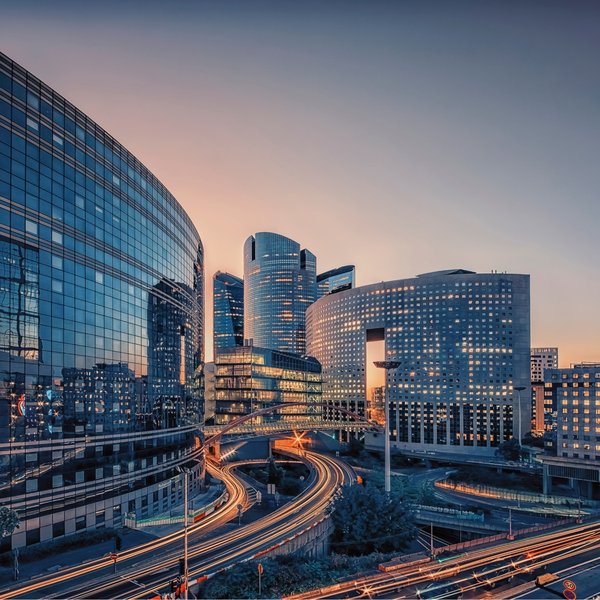 Modern business district with illuminated skyscrapers and light trails at dusk